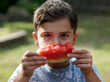 young boy bites into a piece of watermelon