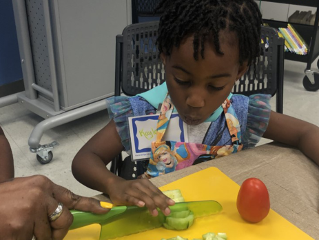 an adult shows a child how to cut vegetables on a cutting board