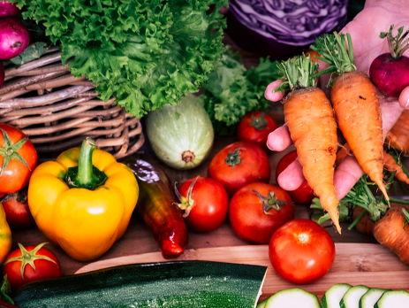 A hand holds carrots and a beet among a spread of other vegetables.
