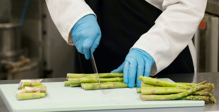 closeup photo of hands chopping asparagus on a cutting board, in an industrial looking kitchen