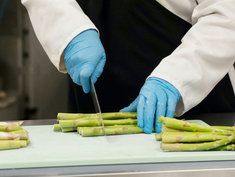 closeup photo of hands chopping asparagus on a cutting board, in an industrial looking kitchen