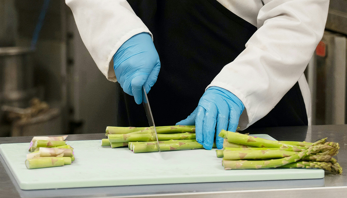 closeup photo of hands chopping asparagus on a cutting board, in an industrial looking kitchen