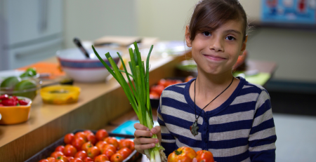 Young child smiles holding vegetables