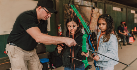 archery instructor shows young girls how to use a crossbow