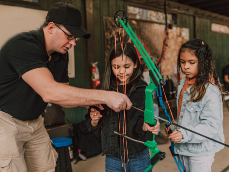 archery instructor shows young girls how to use a crossbow