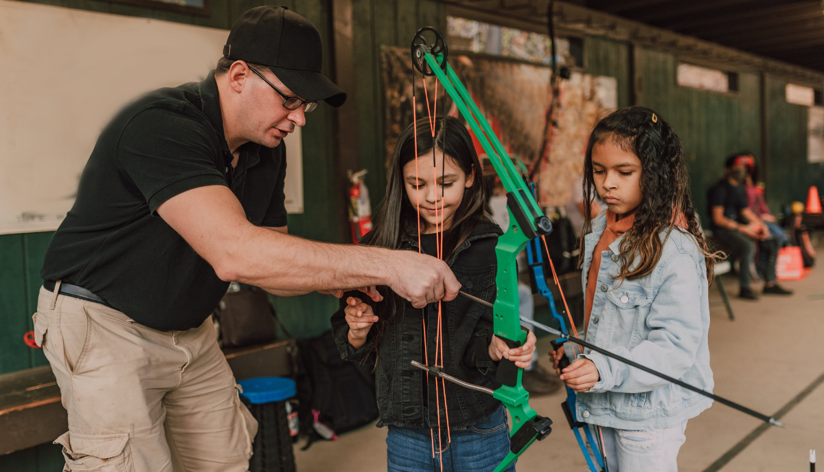 archery instructor shows young girls how to use a crossbow