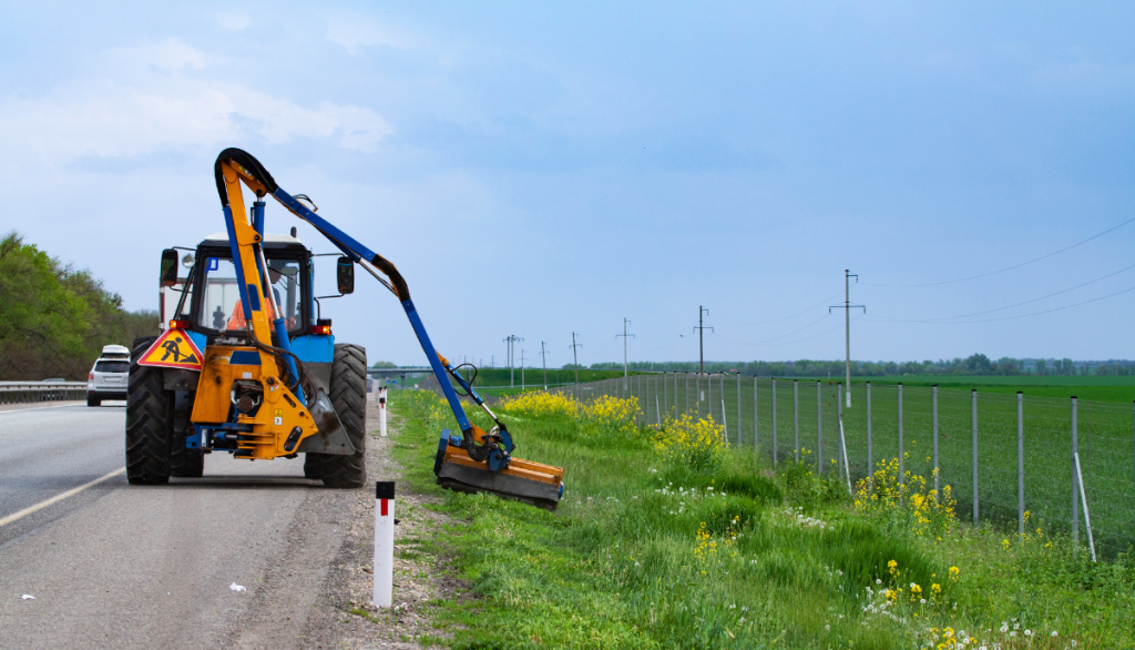 tractor with a mechanical mower mowing grass on the side of the asphalt road