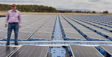 Mike Popp stands on a floating solar array with trees and mountains in the background.