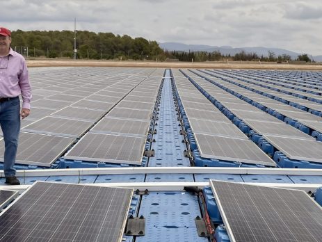Mike Popp stands on a floating solar array with trees and mountains in the background.