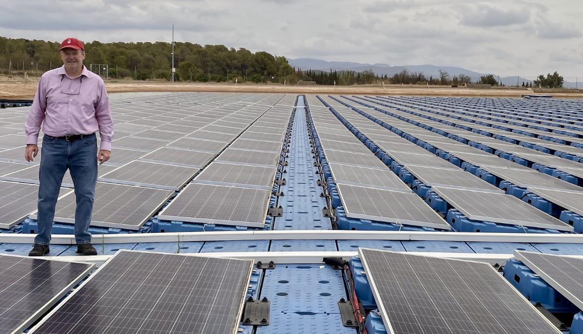 Mike Popp stands on a floating solar array with trees and mountains in the background.