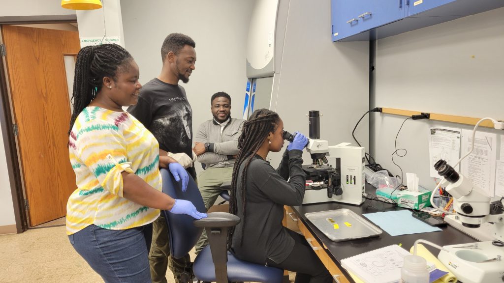 students and faculty examine samples under a microscope