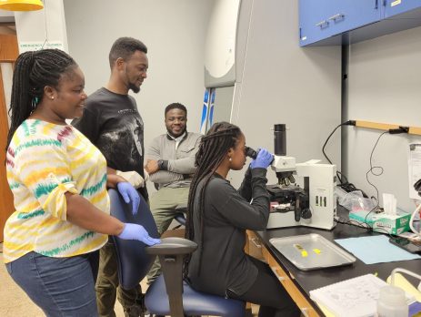 students and faculty examine samples under a microscope