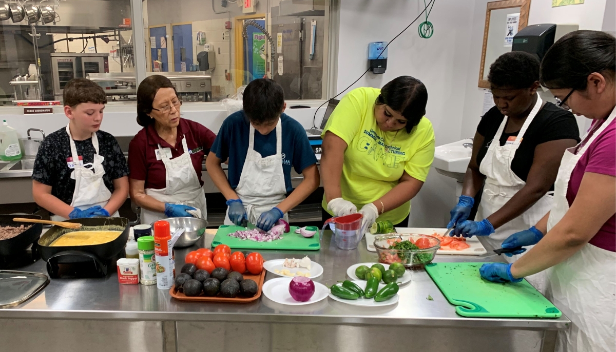 a group of youth and an instructor cook in an industrial kitchen