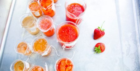 Multiple glass containers with orange and red fruit liquids in them sit on a table.