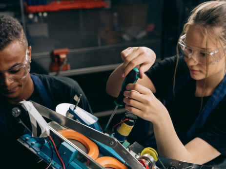 two teens wearing goggles and using tools in a workshop setting