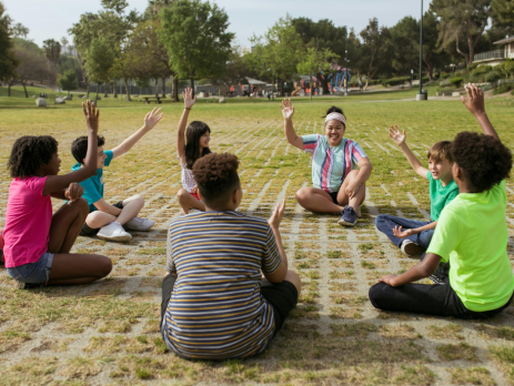 a group of campers sit in a circle with their hands raised