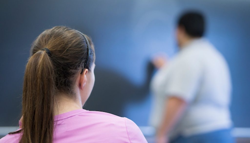 a young girl watches an instructor writing on a blackboard