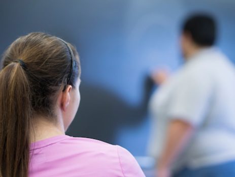 a young girl watches an instructor writing on a blackboard