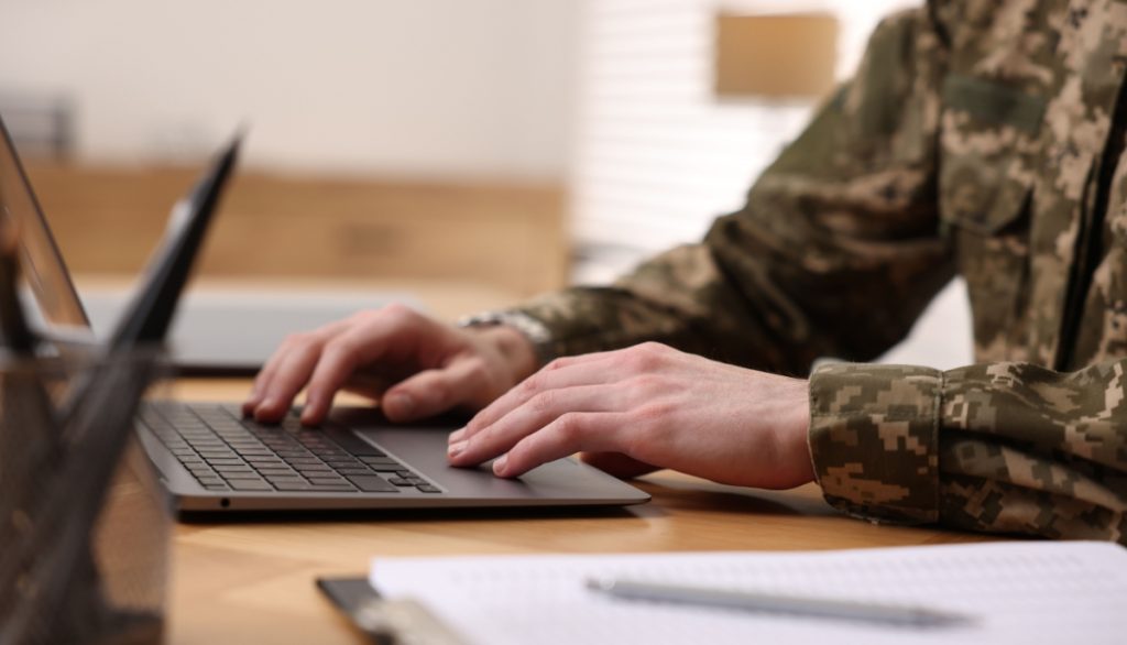 Soldier working with laptop at wooden table indoors