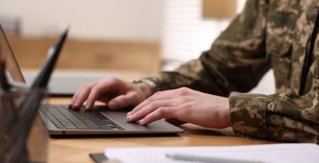 Soldier working with laptop at wooden table indoors